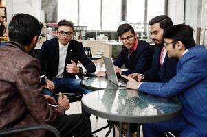 grupp av fem indisk affärsman i kostym sitter på kontoret på café och tittar på laptop. foto