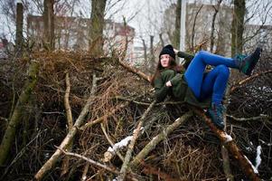 ung flicka bär på lång grön tröja, jeans och svarta huvudbonader vid grenar av tallen i vinterdag. foto