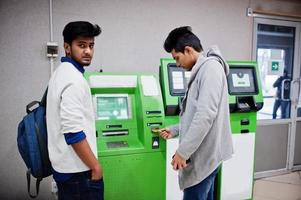 två asiatiska killar tar bort pengar från en grön bankomat. foto