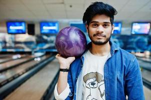 elegant skägg asiatisk man i jeansskjorta stående vid bowlinghall med boll till hands. foto