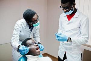 afrikansk amerikansk man patient i tandläkarstol. tandläkare kontor och läkare praktik koncept. professionell tandläkare som hjälper sin patient vid tandläkare. injektionsbedövningsmedel. foto