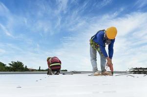 byggnadsarbetare i arbetskläder installerar nya takverktyg takverktyg, elektrisk borr, och användning på nya trätak med plåt. foto