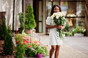 vacker afrikansk amerikansk tjej håller bukett vita rosor blommor på dejting i staden. svart affärskvinna med massa blommor. foto