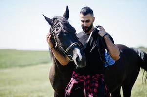 arabiskt högt skägg man bär i svart med arabisk häst. foto