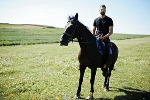 arab högt skägg man bär i svart och solglasögon rida arabisk häst. foto