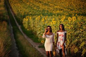 två vackra unga svarta vänner kvinna bär sommarklänning poserar i ett solrosfält. foto