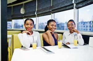 tre afrikansk kvinna i klänning poserar på restaurang, läs menyn. foto