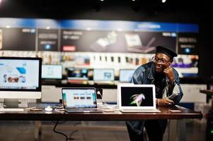 snygg casual afroamerikansk man på jeansjacka och svart basker mot ny bärbar datorskärm på elektronikaffär. foto