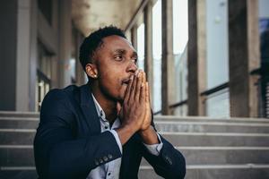 manlig kontorsarbetare trött efter jobbet, afroamerikaner har svår huvudvärk, sitter foto