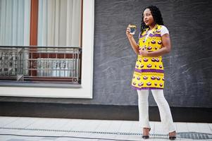 snygga afroamerikanska kvinnor i gul jacka poserade på gatan med varm dryck i engångspappersmugg. foto