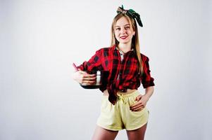 ung rolig hemmafru i rutig skjorta och gula shorts pin up stil med kastrull och kök sked isolerad på vit bakgrund. foto