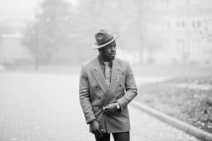 snygg afrikansk amerikansk man modell i grå jacka slips och röd hatt på dimma dag. svartvitt foto. foto