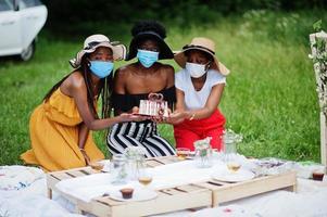 grupp afroamerikanska tjejer med ansiktsmasker som firar födelsedagsfest utomhus med inredning under coronavirus pandemi. foto