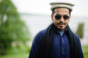 snygg pakistansk indisk muslimsk arabisk man i kurta dhoti-kostym, traditionell pakolhatt och solglasögon. foto