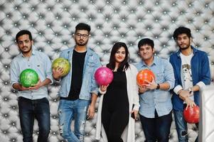 grupp av fem sydasiatiska folk som har vila och kul på bowlingklubben, poserar mot silverväggen med bollar vid händerna. foto