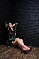 porträtt av en fantastisk ung kvinna i blommig klänning som sitter i den mörka studion. foto