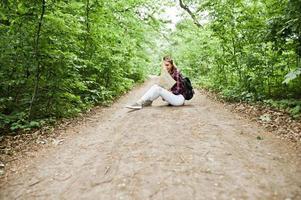 porträtt av en positiv ung vacker blondin som sitter på marken med en karta i händerna i skogen. foto
