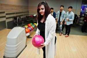 sydasiatisk kvinna står vid bowlinghall med boll på händerna. flickan förbereder sig för ett kast. foto