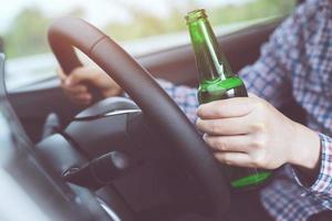 närbild hand berusad ung man medan du kör bil med en flaska öl. drick och kör inte koncept. körning i onykterhet kan faran vara dödsfall. foto