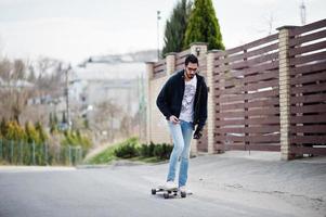 street style arabisk man i glasögon med longboard longboarding på vägen. foto