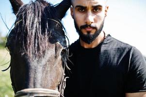 arabiskt högt skägg man bär i svart med arabisk häst. foto