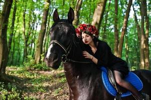 mystisk flicka i krans slitage i svart på häst i trä. foto