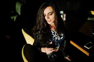 ung lockig kvinna som njuter av sitt vin i en bar. foto