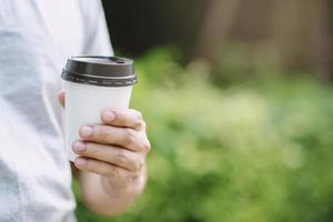 hand som håller papperskopp med take away dricker kaffe på naturligt morgonsolljus. plats för din logotyp. lämna utrymme för att skriva text. foto