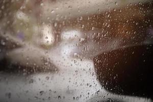 bilfönster med regndroppar fönster på glasbackspegel med suddig bakgrund. stadsliv på kvällen under regnperioden storm regnar. vänligen kör bil försiktigt koncept, hala vägar. mjukt fokus. foto