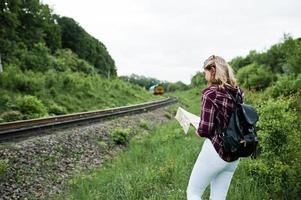 porträtt av en ung blondin i tartanskjorta bredvid tåget med en karta. foto