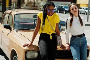 vit kaukasisk tjej och svart afroamerikan tillsammans mot gamla retrobil. världsenhet, raskärlek, förståelse i tolerans och samarbete mellan raser och mångfald. foto