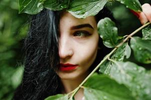 närbild porträtt av sensuell brunett flicka med röda läppar. goth dramatisk kvinna vid trädgren. foto