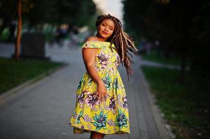 söt liten höjd afroamerikansk flicka med dreadlocks, bär på färgad gul klänning, poserade vid solnedgången. foto