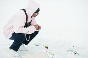 afrikansk amerikansk fiskare med fiskespö sitter på frusna havet. vinterfiske. foto