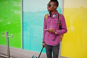 afrikansk amerikansk man i rutig skjorta, solglasögon och jeans med resväska och ryggsäck. svart man resenär. foto