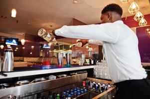 afroamerikansk bartender som arbetar bakom cocktailbaren. beredning av alkoholhaltiga drycker. foto