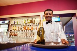 afroamerikansk bartender i baren håller champagne med glas på bricka. foto