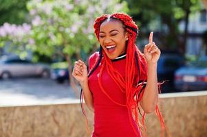 söt och smal afrikansk amerikansk flicka i röd klänning med dreadlocks i rörelse som har roligt på gatan. stilren svart modell. foto