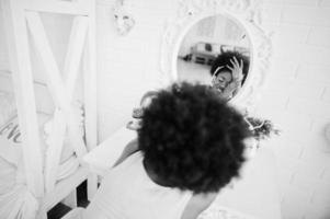 ung afroamerikansk kvinna tittar i spegeln och lyssna på musik i hörlurar. foto
