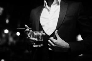 närbild hand av stilig välklädd arabisk man med glas whisky och cigarr poserade på puben. foto