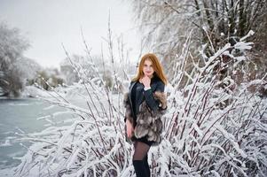 rödhårig tjej i päls som går på vinterns snöiga park. foto