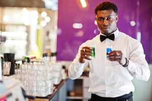 afroamerikansk bartender i baren håller två cocktail shots. beredning av alkoholhaltiga drycker. foto