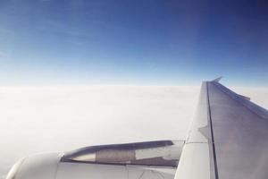 flygplansvingevy. tittar genom fönstret på ett flygplan under flygning i vinge med en blå himmel plan. flygande i himlen och havet av moln. transport resor koncept. mjukt fokus foto