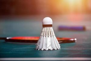 badmintonfjärdeboll och racket med neonljusskuggning på grönt golv i inomhusbadmintonbana, suddig badmintonbakgrund, kopieringsutrymme. foto