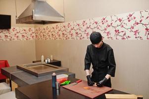 professionella kockkläder i svart gör sushi och rullar i ett restaurangkök med japansk traditionell mat. foto