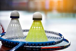 vit och gul plastbadmintonfjärdeboll och racket med neonljusskuggning på grönt golv i inomhusbadmintonbana, suddig badmintonbakgrund, kopieringsutrymme. foto