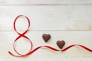 rött gåva firande band viftade i form av nummer 8 och choklad i hjärtform på vit trä bakgrund. gratulationskort med kopia utrymme för 8 mars, internationella kvinnodagen foto