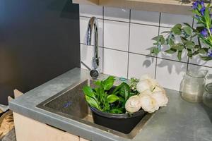 tvätta metall diskbänk och olika glasburkar på metall bord bredvid korg med blommor. blomsteraffärsarrangemang foto