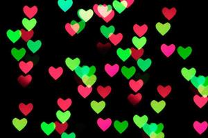 mångfärgade hjärtan bokeh av rosa och gröna färger på svart bakgrund. textur för semester foto