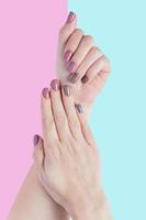 vacker ung kvinnas händer isolerade på pastellrosa och blå bakgrund. snygg trendig kvinnlig manikyr med grått, rosa och brunt nagellack. foto